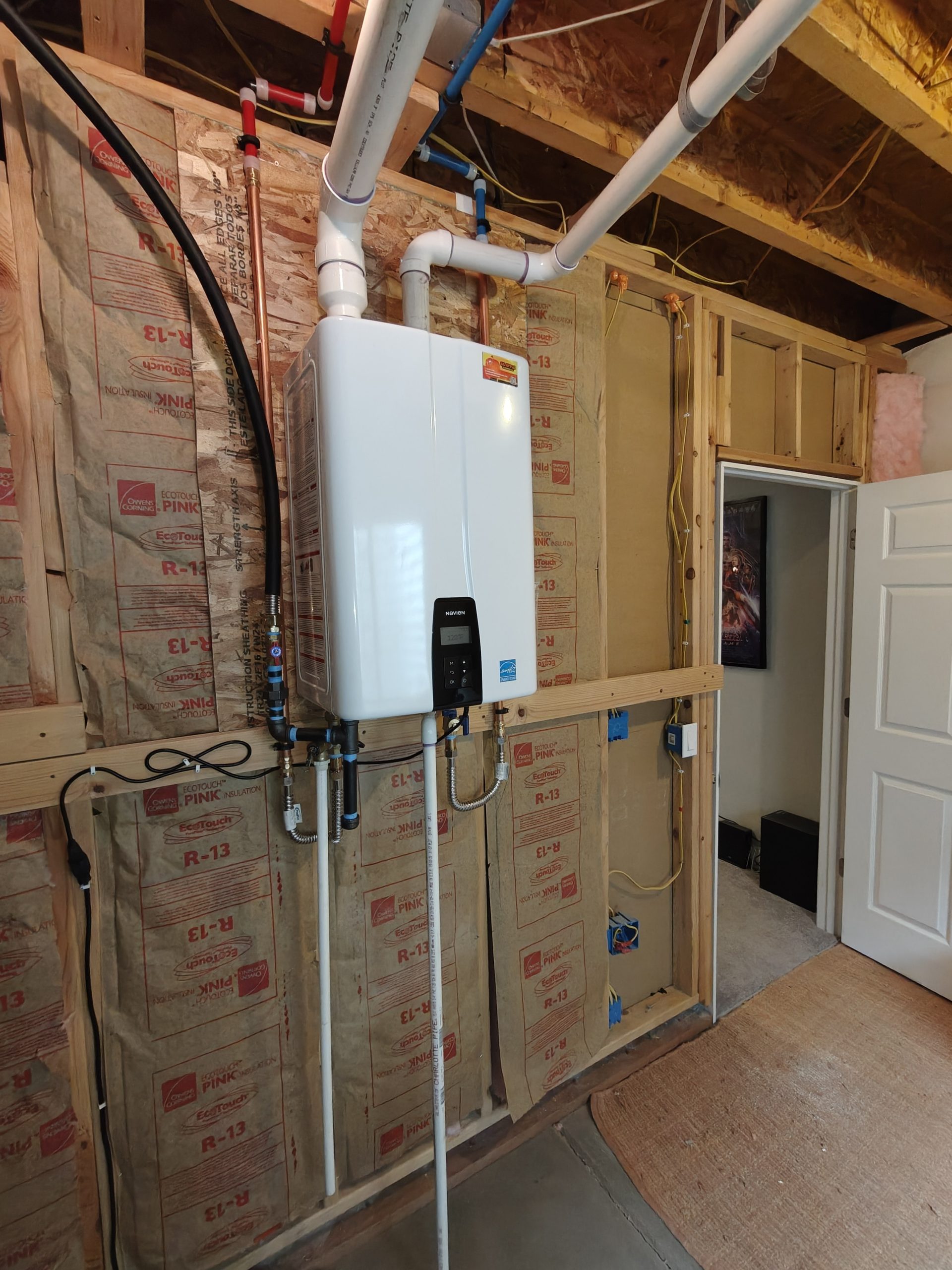 Wall-mounted Navien tankless water heater installed with white PVC venting over pink insulation in a Westminster, CO basement.